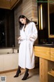 A woman in a white robe standing in a bathroom.