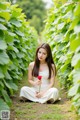 A woman in a white dress holding a red rose in a vineyard.