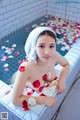 A woman in a bathtub with rose petals on the floor.