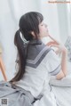 A woman in a school uniform sitting on a bed.