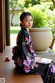 A woman in a black kimono sitting on a wooden bench.