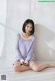 A woman sitting on a bed wearing a purple sweater.