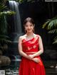 A woman in a red dress standing in front of a waterfall.